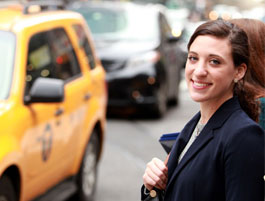 A woman in a navy blazer stands on a busy city street, with yellow taxis and cars in the background, capturing an urban scene.