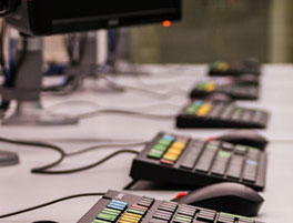A row of computer keyboards with colorful function keys and mice, set up on a desk in a modern workspace.