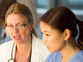 Two healthcare professionals in scrubs and a lab coat engaged in a discussion, emphasizing teamwork and collaboration in a medical setting.