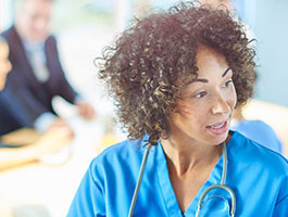 A nursing student in a blue scrubs with a stethoscope around their neck, seated in a modern medical lab..
