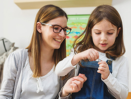 A female teacher and a child engaged in a hands-on activity together, smiling and focused in a bright, friendly environment with colorful decor.