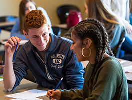 Two students collaborate at a table, reviewing notes and working on assignments in a classroom setting.