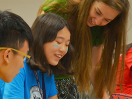 A group of young people engaged in a collaborative activity, seated around a table, with vibrant clothing and focused expressions.