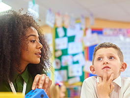 A teacher engages with a student in a colorful classroom filled with educational posters and materials.